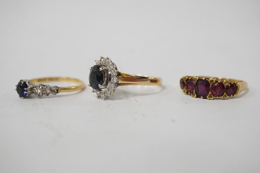 A group of three rings, comprising: a sapphire and diamond cluster ring, size M1/2, stamped 14K and 585; a five-stone ring set with cushion-shaped garnets and rose-cut diamonds, size L; and a synthetic sapphire and simul